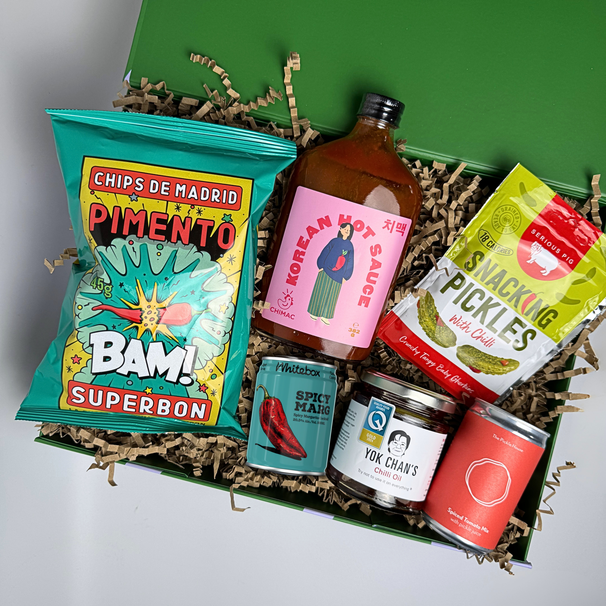 Assorted snack items including chips, hot sauce, and pickles in a green box.