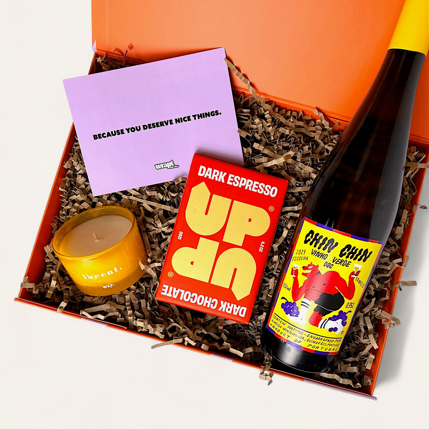 Gift box with a bottle, candle, and chocolate bar on a white background