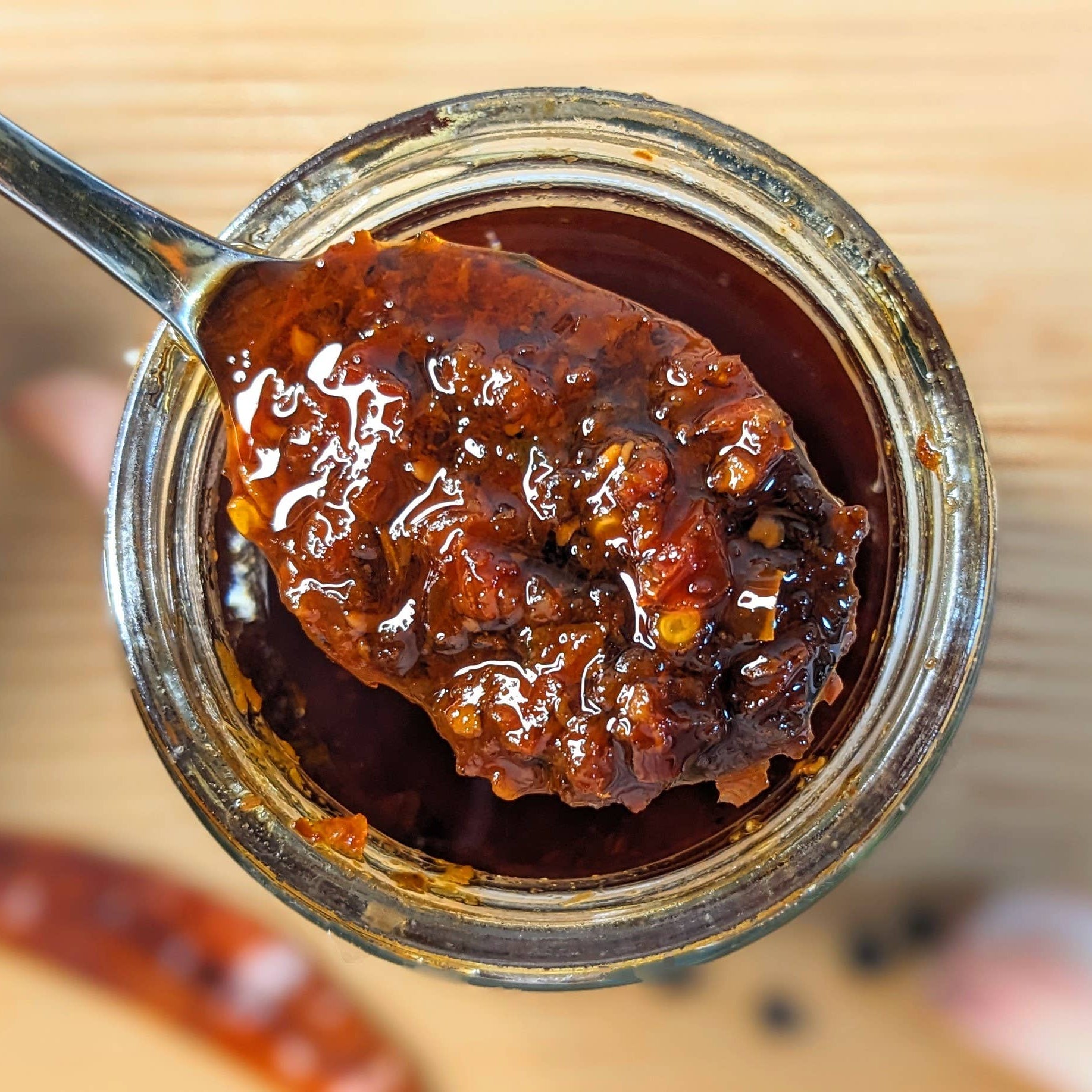 Jar of dark brown jam with a spoonful being lifted, on a wooden surface.